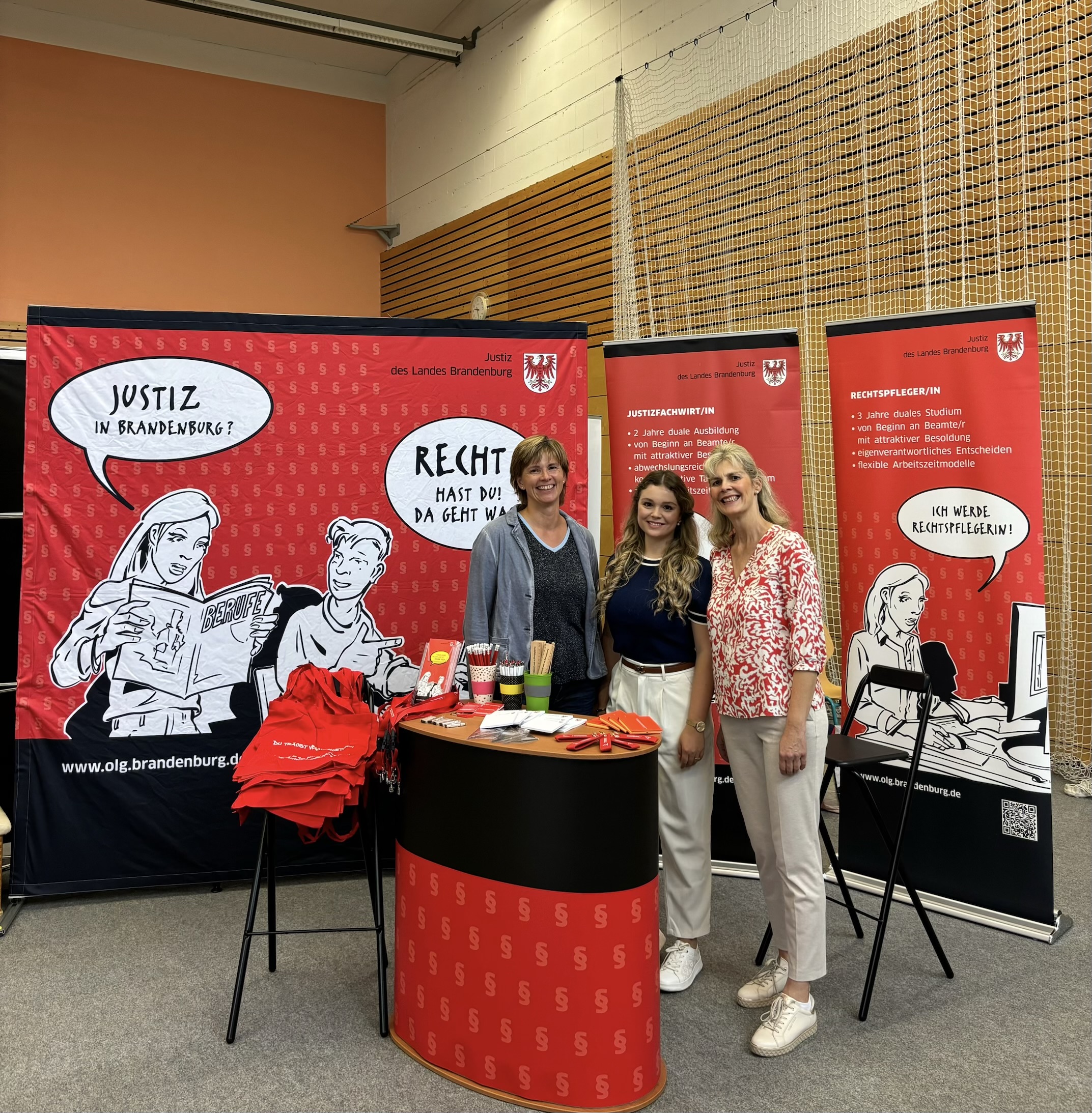 drei Frauen stehen hinter einem Tresen auf einer Bildungsmesse und lächeln in die Kamera